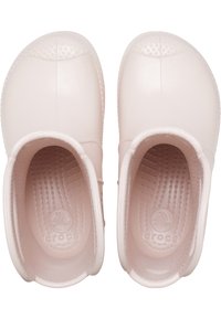 Jasnoróżowe Crocsy o gładkiej, teksturowanej powierzchni, z zaokrąglonym noskiem i wypukłymi kropkami na wierzchu. Wnętrze posiada prążkowany wzór.