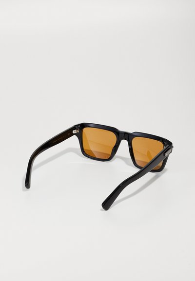 Lunettes de soleil rectangulaires noires avec des verres orange, dotées d'une finition brillante et de branches épurées. Détail matériel remarquable près des charnières.