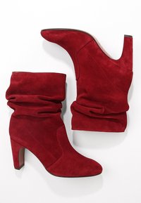 Botas de tobillo de ante rojo con punta afilada, diseño holgado y un tacón de 3,5 pulgadas. Textura suave y detalles de costura sin costuras.