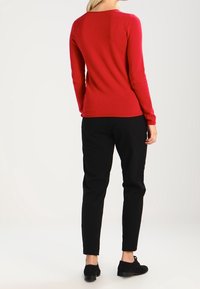 Czerwony sweter z długim rękawem wykonany z miękkiego materiału, zestawiony z czarnymi zwężającymi się spodniami i czarnymi butami. Prosty design o dopasowanej sylwetce.