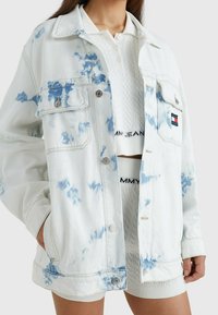 Hellblaue Jeansjacke mit einem Batikmuster in Blau, zwei vorderen Taschen, Metallknöpfen und einem Markenpatch auf der Brusttasche.