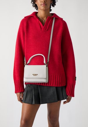 Suéter rojo de punto con cuello y puños acanalados, combinado con una falda de cuadros negra con pliegues. Un bolso blanco con asa superior y correa para el hombro.