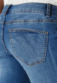 Jeans i middels blå med en glatt tekstur, med en baklomme og kontrasterende sømmer langs sømmene og midjebåndet.