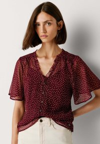 Blouse en voile bordeaux à pois blancs, col en V avec bordure à volants, manches courtes volantées, boutonnée devant, coupe décontractée.
