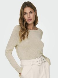 Strickoberteil mit langen Ärmeln in Hellbeige, mit einem lockeren Schnitt und rundem Ausschnitt. Dazu hohe, cremefarbene Hosen mit breitem Gürtel.