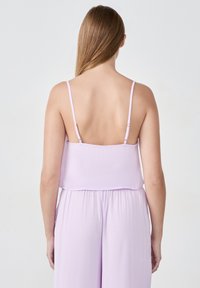 Liliowy top na ramiączkach z cienkimi regulowanymi paseczkami, o luźnym kroju i gładkiej tkaninie. Tył jest otwarty, co podkreśla prosty, elegancki design.