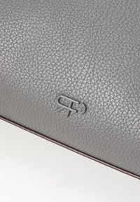 Grå struktureret læderpung med et præget logo. Har et slankt design og en struktureret form, der understreger både holdbarhed og elegance.