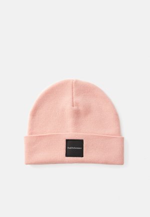 Roze gebreide beanie met een omgeslagen rand, voorzien van een zwart vierkant label met witte tekst. Zachte textuur en afgeronde topvorm.