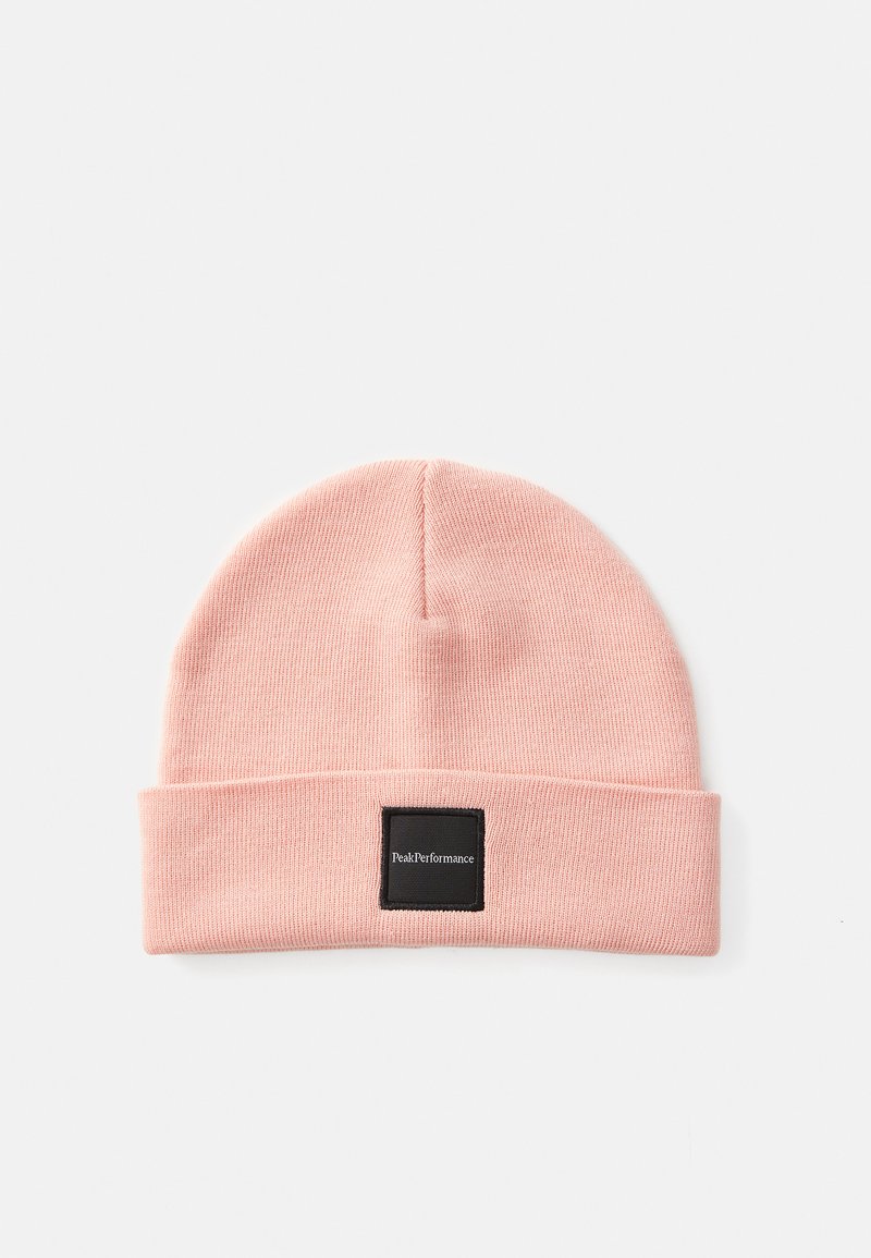 Roze gebreide beanie met een omgeslagen rand, voorzien van een zwart vierkant label met witte tekst. Zachte textuur en afgeronde topvorm.