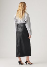 Jupe en cuir noir à taille haute, finition texturée et poches arrière. Associée à une chemise rayée et des talons noirs.