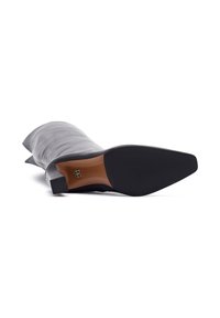 Botte en cuir noir montante avec un bout pointu, une silhouette épurée et un petit talon carré. La semelle présente une finition en caoutchouc.