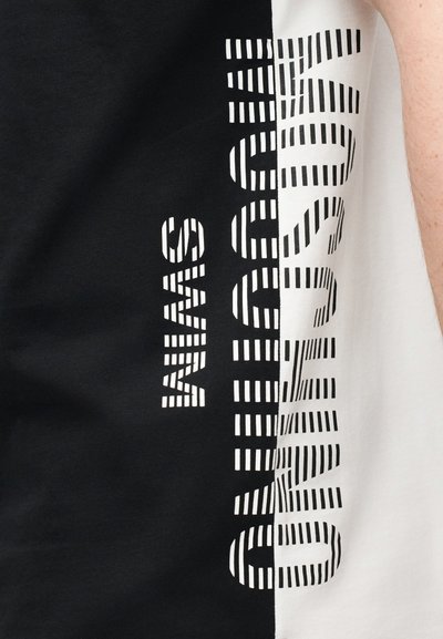 Tissu bicolore noir et blanc divisé verticalement avec le texte "MUNICH SWAN" en motif rayé le long de la séparation, faisant partie d'un vêtement porté par une personne.