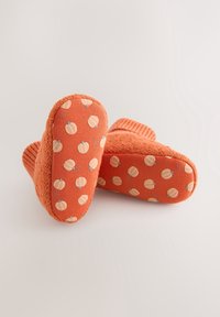Chaussettes orange douces pour tout-petits avec des motifs de citrouille sur les semelles, des poignets tricotés et un corps texturé, sur un fond uni.