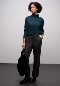 Sininen pooloneule, istuva ja pitkähihainen. Harmaat räätälöidyt housut, joissa kaksi etutaskua ja nappikoristeet. Musta laukku kädessä.