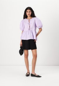 Lilla puff-sleeve topp med en nøkkelhullsdetalj og snøring, sammen med en svart mini-skjørt og svarte leiligheter med hullmønster.