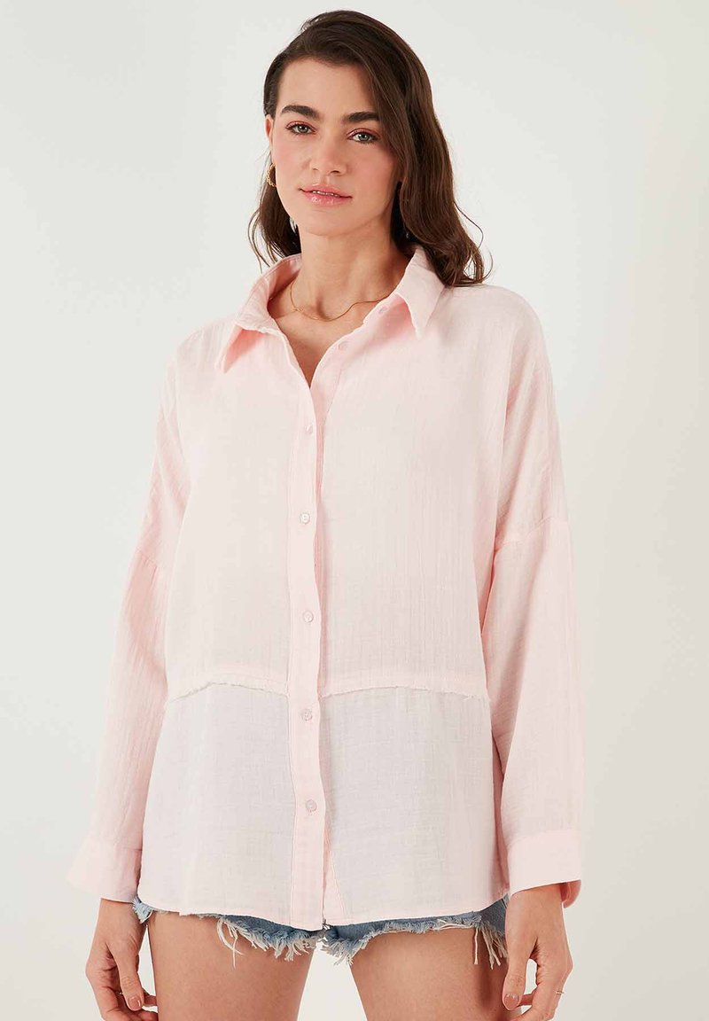 Light pink button-up shirt with a soft, textured fabric, featuring a straight cut, long sleeves, and a split design at the waist.