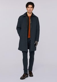 Tmavě modrý kabát s límečkem, nošený přes černou koženou bundu a oranžový polo. Ladící tmavé kalhoty a hnědé boty.