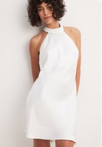 Vestido blanco de satén con tirantes al cuello, con un corsé ajustado y un dobladillo acampanado, que muestra una textura suave y brillante con líneas limpias.