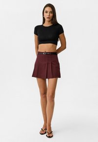 Zwarte aansluitende crop top, bordeaux plisségedeelte met een riem, platte sandalen, gladde stof en een schoon ontwerp tegen een neutrale achtergrond.