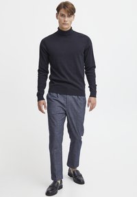 Mørk marineblå strikkegenser kombinert med mønstrede grå bukser. Genseren har en slim fit, mens skoene er sorte skinnloafers.