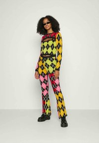 Conjunto composto por duas peças, apresentando uma blusa de mangas longas e calças ligeiramente largas, feito de um tecido texturizado com um padrão argyle em rosa, amarelo, verde e preto.