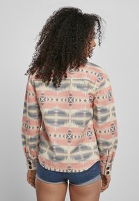 Langærmet skjorte med et flerfarvet geometrisk mønster i pink, beige og blå. Lavet af stof; har knapdetaljer og buet kant.