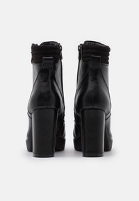 Bottines en cuir noir avec un talon bloc haut, un col texturé à nervures et une fermeture éclair à l'arrière. Fini lisse et forme structurée.
