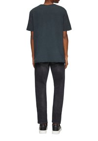 Donkergrijze katoenen t-shirt met korte mouwen, met een relaxte pasvorm en zichtbare stiksels aan de onderkant. Gecombineerd met zwarte broeken en witte schoenen.