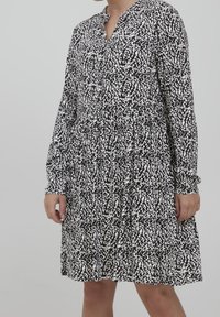 Mekko, jossa on pitkät hihat ja musta-valkoinen kuvio, varustettuna kauluksella ja rypytetyllä vyötäröllä, valmistettu kevyestä kankaasta.