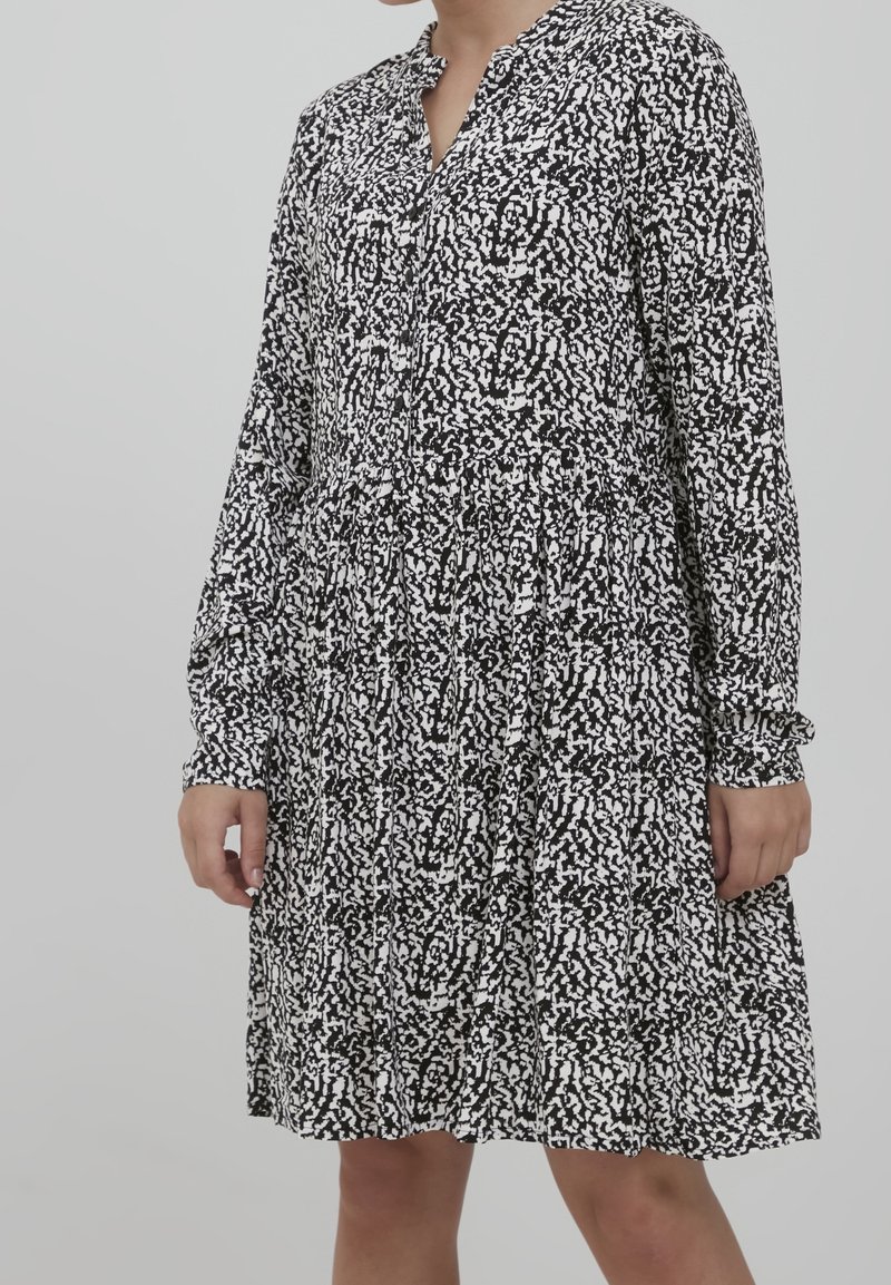 Mekko, jossa on pitkät hihat ja musta-valkoinen kuvio, varustettuna kauluksella ja rypytetyllä vyötäröllä, valmistettu kevyestä kankaasta.