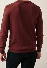 Pull en maille bordeaux avec poignets et ourlet côtelés, mettant en valeur des accents texturés aux épaules, un tissu lisse et une silhouette ajustée.