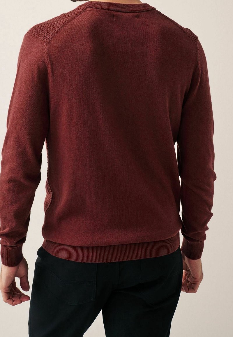 Pull en maille bordeaux avec poignets et ourlet côtelés, mettant en valeur des accents texturés aux épaules, un tissu lisse et une silhouette ajustée.
