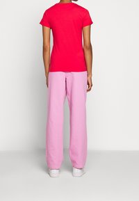 Camiseta roja de manga corta combinada con pantalones de pierna ancha rosa claro. La tela parece suave y ligera, con un diseño sencillo. Incluye zapatillas blancas.