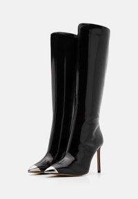 Stivali al ginocchio in pelle verniciata nera con punte argentate a forma di punta e tacchi a stiletto, mostrati in posizione angolata su uno sfondo bianco.