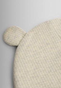 Okrúhly vankúš so žíhanou, krémovo bielou látkou. Má dva malé zaoblené ušká. Mäkká textúra; minimalistický dizajn.