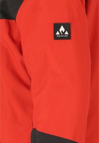 Rote Stoffjacke mit schwarzen Akzenten, glatter Textur und einem quadratischen Logopatch mit einem Bergdesign, das am Ärmel angebracht ist.