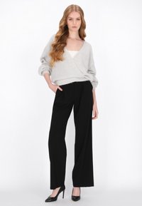 Grijze oversized gebreide trui met een V-hals, gecombineerd met hoge zwarte wijde broek en zwarte high heels.