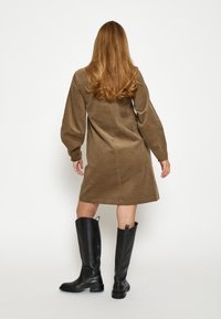 Braunes Cordkleid mit langen Ärmeln und einer locker sitzenden Passform, kombiniert mit schwarzen kniehohen Lederstiefeln mit einem dicken Absatz.