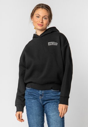Black fleece hoodie with a relaxed fit, featuring a front pocket and white printed text design. Paired with blue denim jeans.