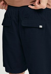 Navy textured shorts with two front pockets, elastic waistband, and a small label. Fabric features a ribbed pattern.