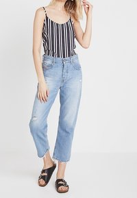 Body blanc et noir rayé associé à un jean taille haute bleu clair avec des détails usés et des ourlets effilochés et courts. Sandales noires.