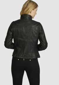 Black leather jacket with a fitted design, high collar, and seam detailing. Shiny finish and slightly flared hem accentuate the silhouette.