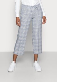 Ljusblå rutiga croppedbyxor med elastisk midja och dragsko. Kombineras med vita sneakers. Mönstret består av korsande linjer.