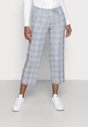 Lichtblauwe geruite cropped broek met elastische tailleband en trekkoord. Gekleed met witte sneakers. Het patroon bestaat uit kruiselings lijnen.