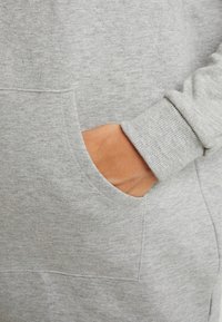 Grå sweatshirt med en texturerad yta, med en framficka och ribbade ärmslut. Materialet verkar mjukt och avslappnat.