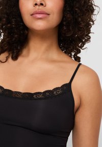 Zwarte cami-top met dunne bandjes, voorzien van kant langs de halslijn. De stof is glad met een rekbare, aansluitende pasvorm.