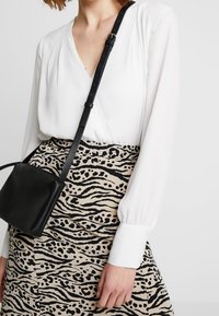 Blusa bianca a scollo a V con maniche lunghe, abbinata a una gonna beige con stampa animale nera. Borsa a tracolla nera. Dettagli in tessuto testurizzato visibili.