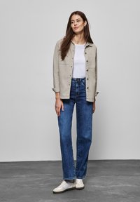 Ljusgrå skjorta över en vit t-shirt, tillsammans med högmidjade blå jeans och beiga skor. Visar en avslappnad passform och en ledig stil.