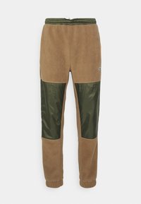 Brown fleece sweatpants with green nylon panels, elastic waistband, drawstring, and cuffs at the ankle. Lacoste logo on the side.