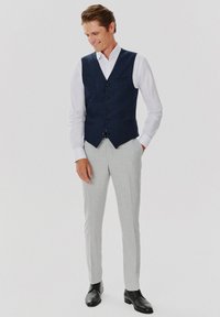 Ciemnoniebieska lniana kamizelka z dekoltem w kształcie V, zapięciem na guziki i kieszonką, połączona z jasnoszarymi spodniami w kant oraz czarnymi eleganckimi butami.